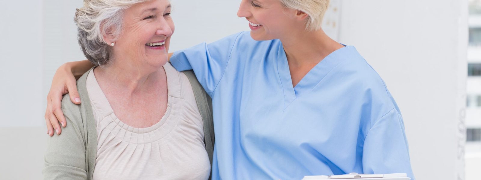 happy-nurse-with-arm-around-senior-patient-clinic-min